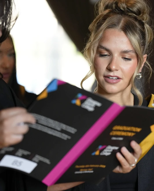 Two female graduates reading through the Glasgow Kelvin College graduation programme together. Two female graduates reading through the Glasgow Kelvin College graduation programme together.